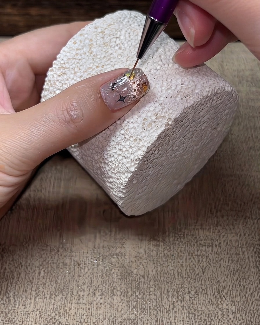 Un pincel delineador fino aplicando top coat duro alrededor de los bordes y huecos de los cristales en una uña terminada.