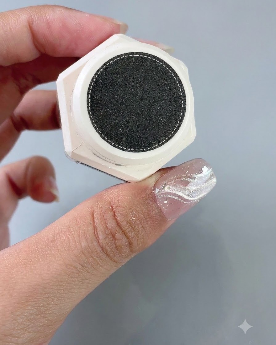 Un envase de gel de estilo texturizado sostenido junto a una uña con una pegatina de guía francesa aplicada.