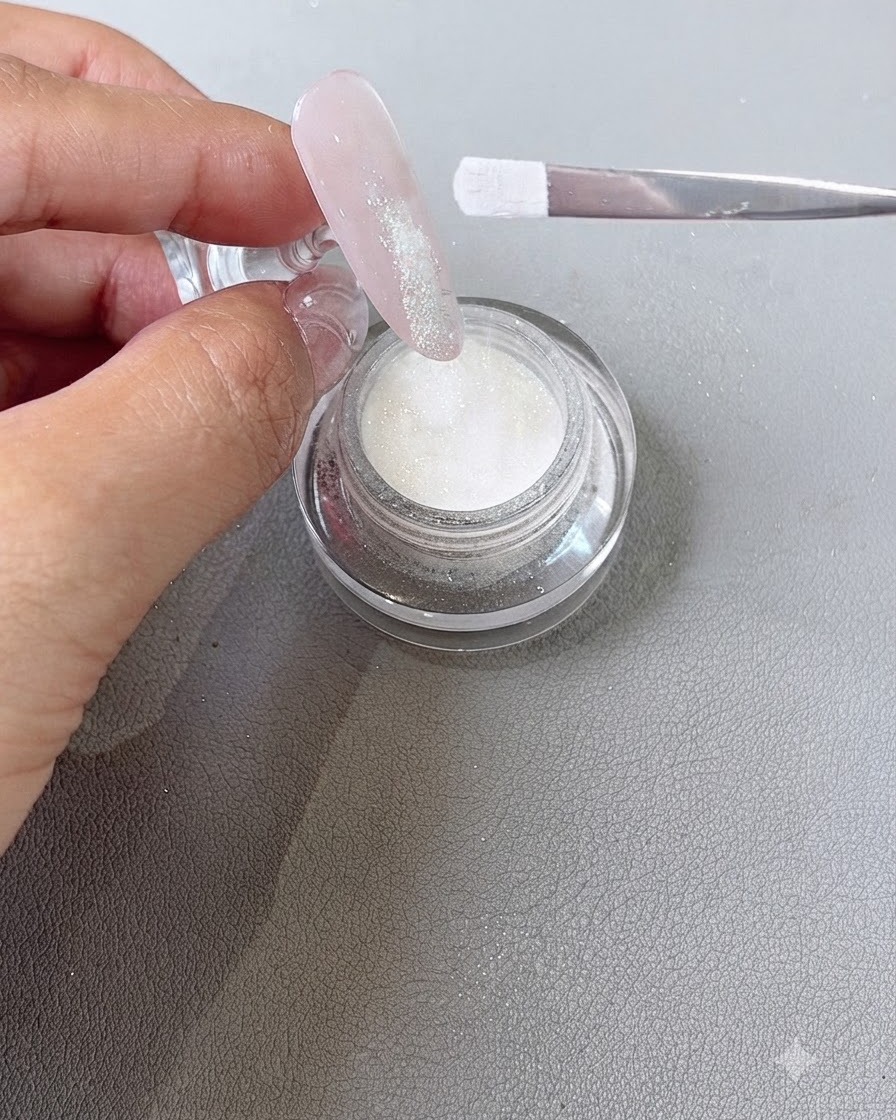 Polvo de inmersión siendo espolvoreado desde un pincel sobre el área de la punta de gel húmedo de una uña.