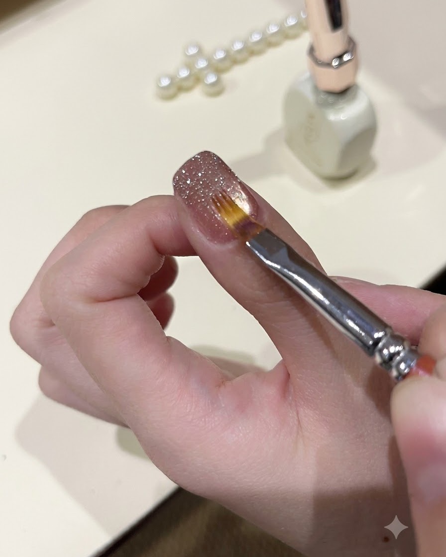 Un pincel fino alisando el gel de purpurina brillante sobre la superficie de una uña esculpida.