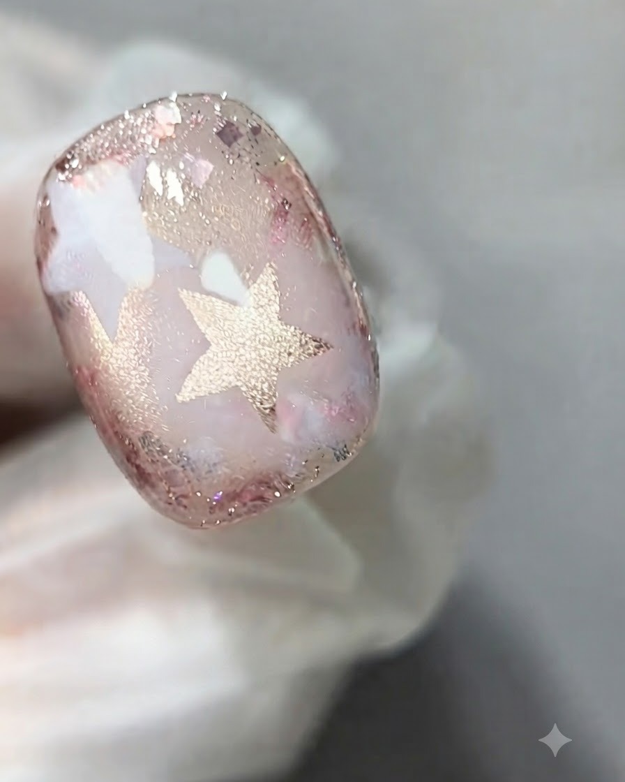 Un pincel de uñas aplicando una capa de gel ojo de gato rosa traslúcido sobre la superficie de una uña decorada.