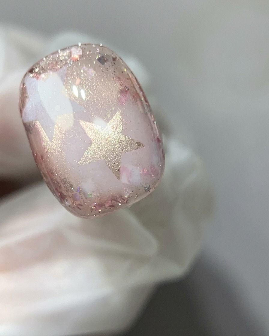 Un imán especializado sostenido sobre una uña de gel ojo de gato rosa para concentrar el reflejo brillante en un efecto de gota de vidrio.