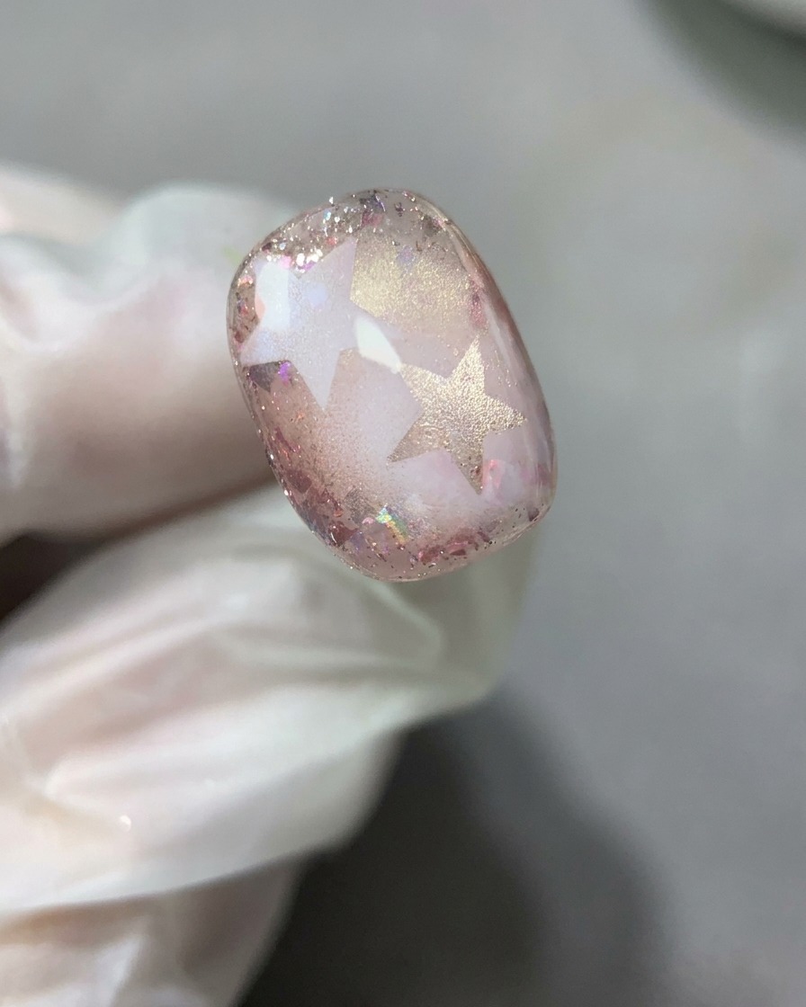Un pincel de uñas esparciendo una capa suave y fina de gel base transparente sobre el diseño completo de estrellas y purpurina.
