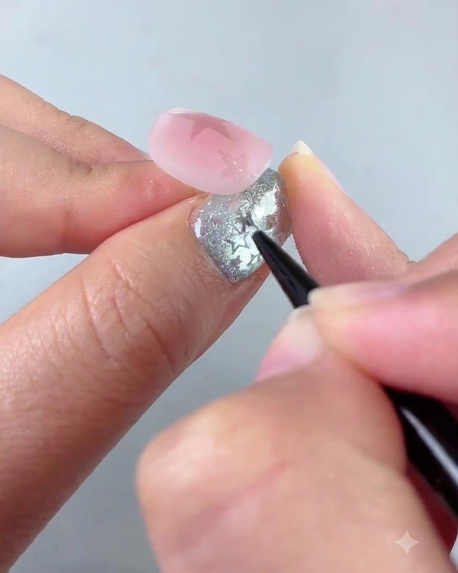 Un pincel delineador detallando una forma de estrella más pequeña cerca de la esquina inferior izquierda de una uña rosa.