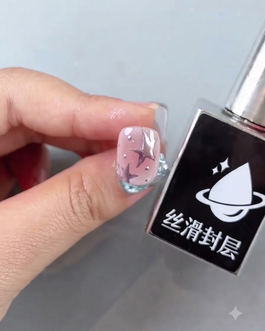 Una botella de capa superior lisa junto a una uña rosa terminada con diseños de estrellas y brillantes acentos plateados.