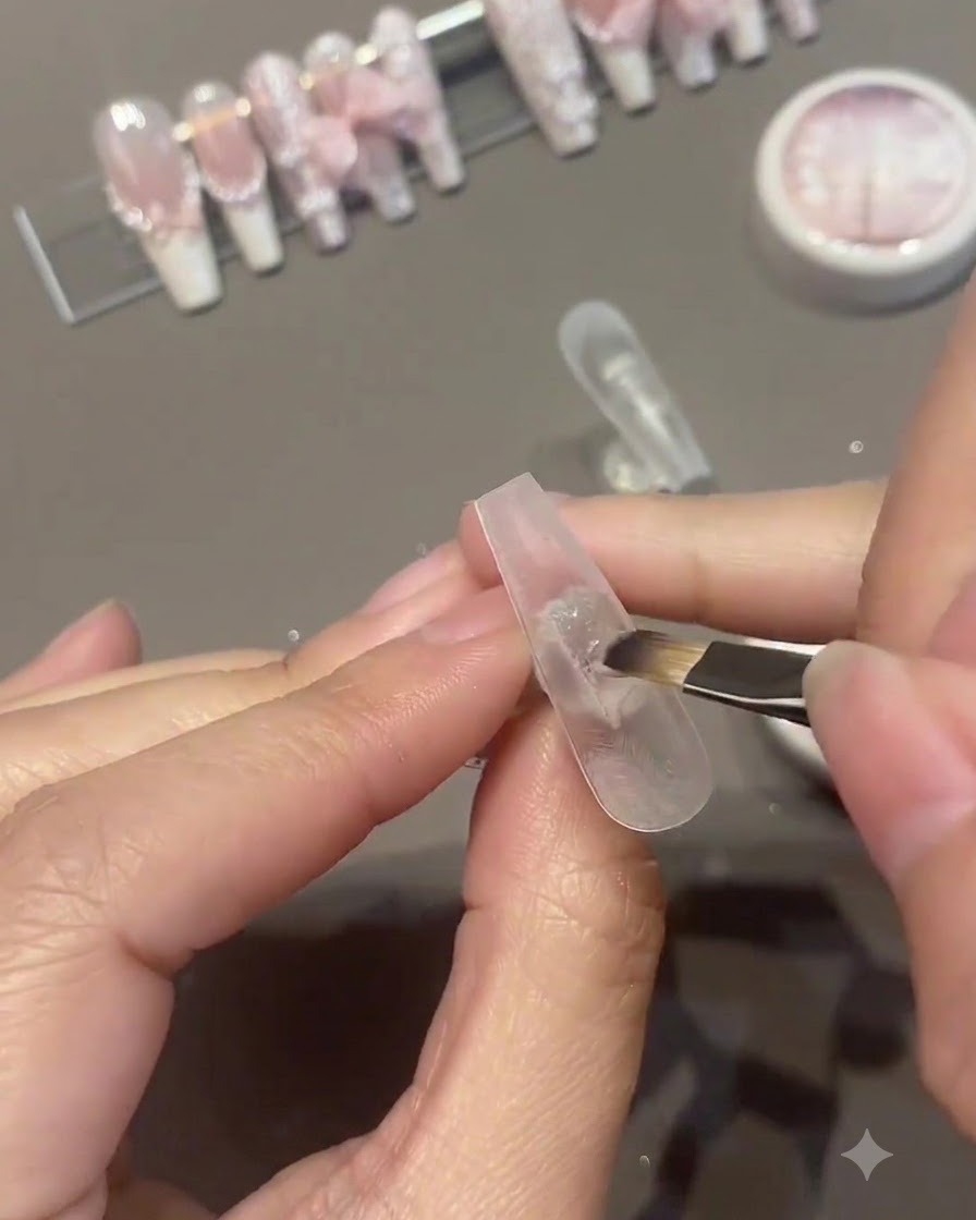 Un pincel aplicando una segunda capa de esmalte de gel rosa sobre la superficie de una uña artificial.