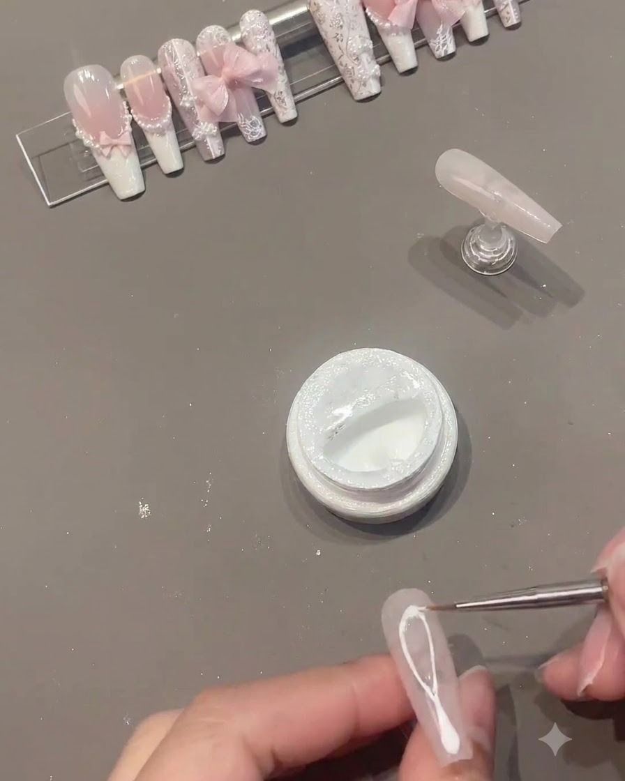 Un pincel delineador fino dibujando líneas de gel de araña blanco a través del centro de una uña de gel rosa.