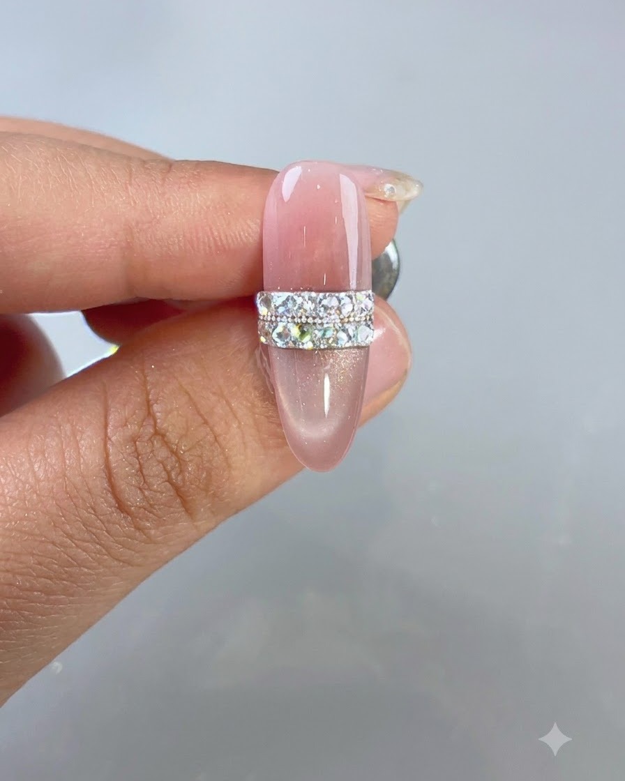 Un diseño de uñas de ojo de gato rosa completado con un motivo de anillo de pedrería y cuentas bajo iluminación de estudio.