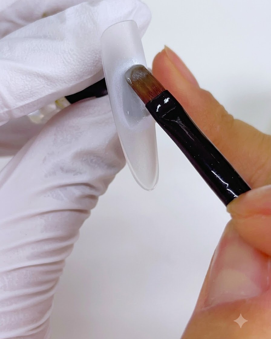 Un pincel aplicando una capa de gel sobre una base circular de perla en una uña.