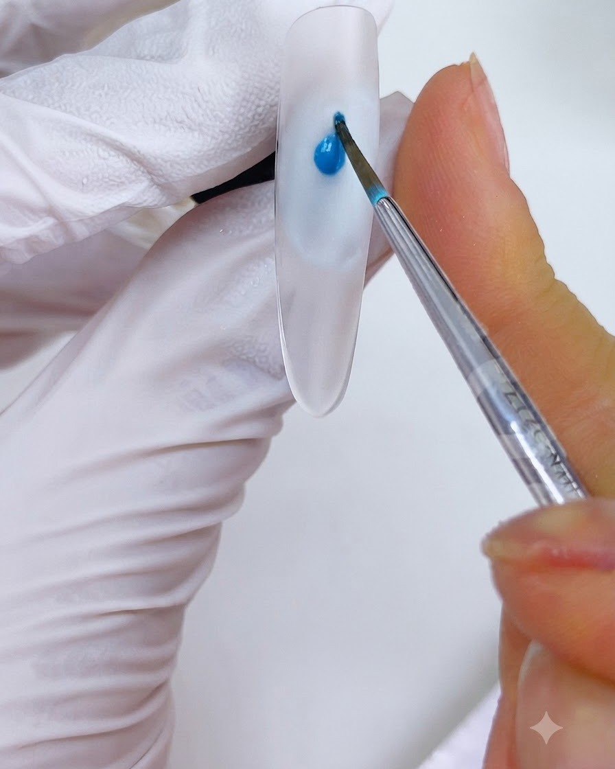 Un pincel fino colocando una gota de tinta azul cielo en un diseño de uñas.