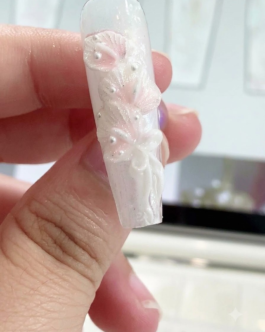 Un bolígrafo moldeador de silicona alisando un nudo de lazo en un diseño de uña esculpido.