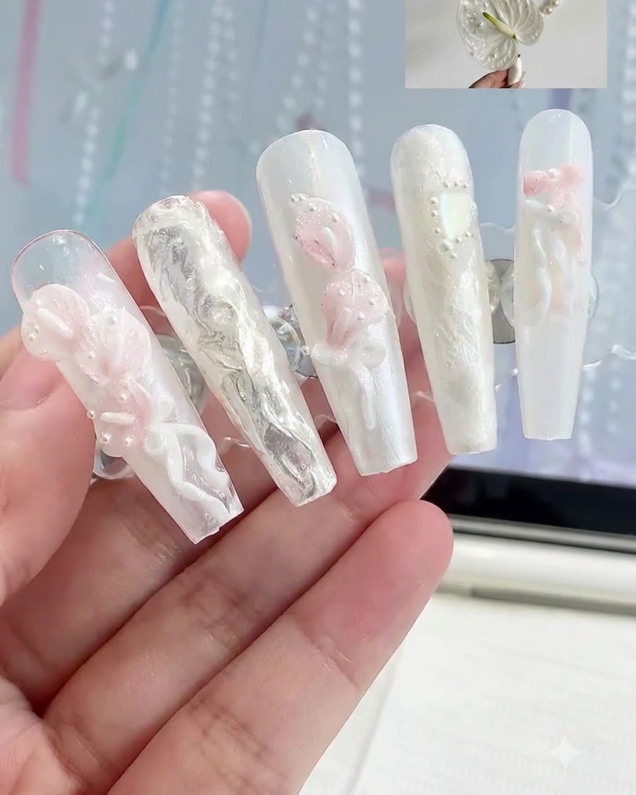 Un soporte de exhibición que sostiene múltiples uñas postizas con varios diseños de nail art floral en 3D blanco y rosa.
