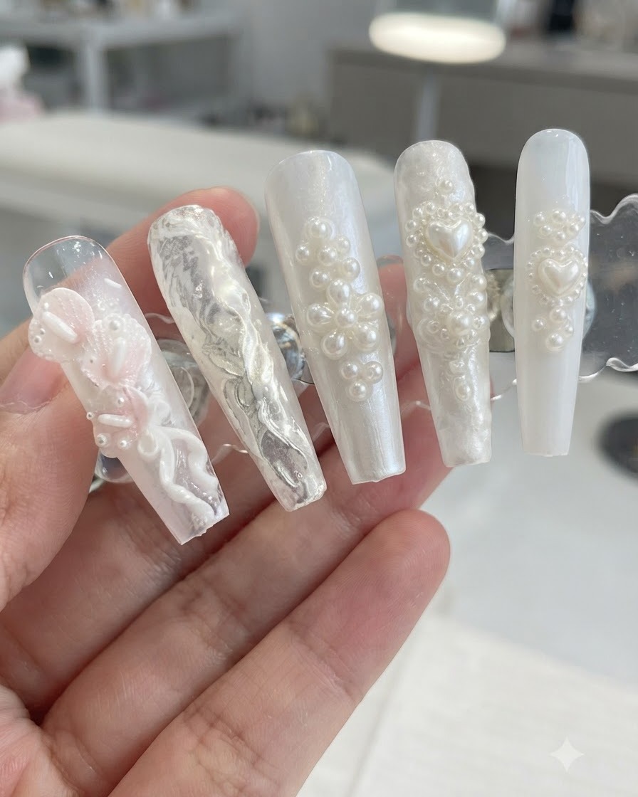 Un soporte de exhibición que muestra diseños de uñas 3D de perlas y flores después de barrer el exceso de polvo brillante.