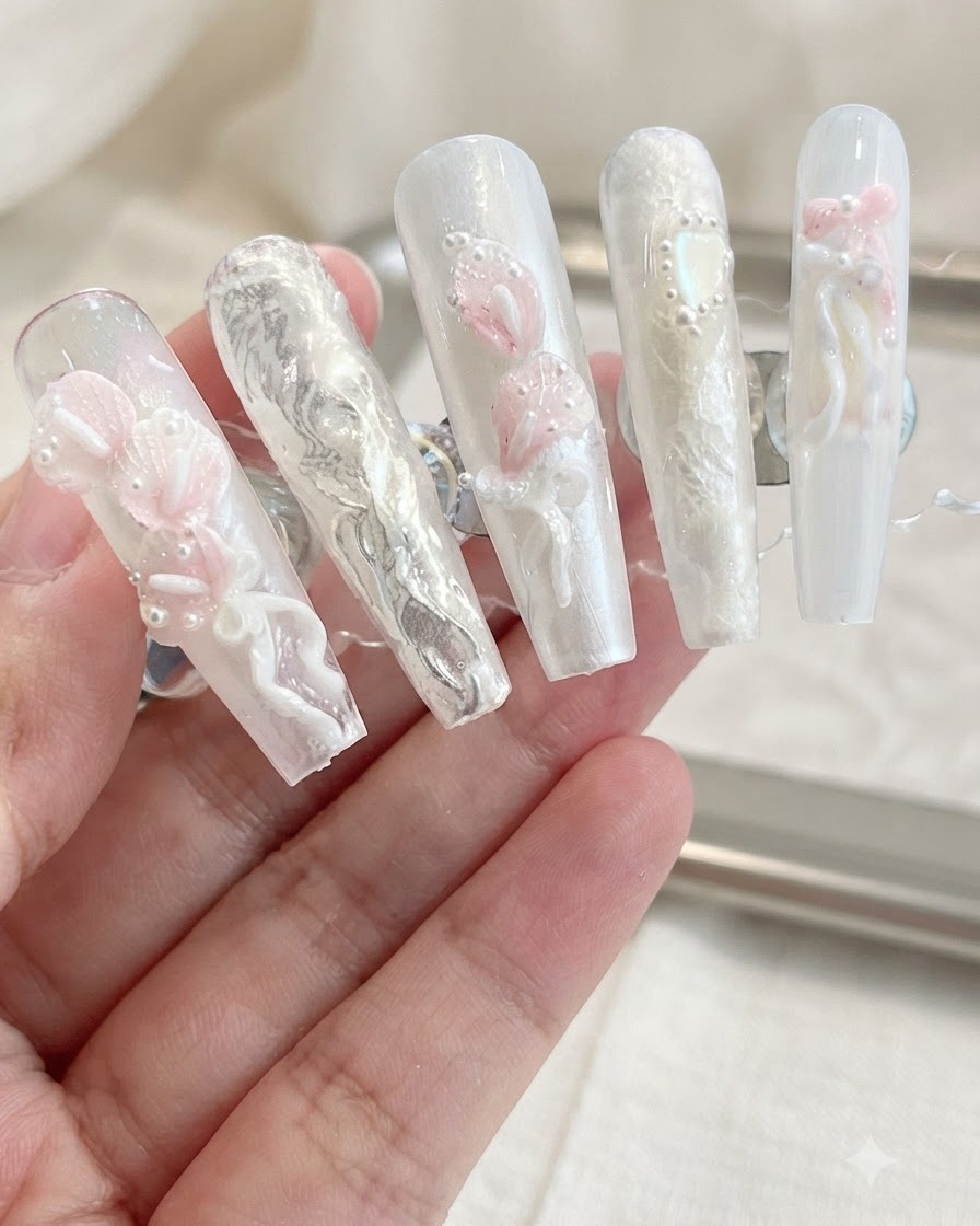 Una exhibición de uñas postizas terminadas que presentan lirios calla en 3D, lazos y adornos de perlas sobre un fondo neutro.