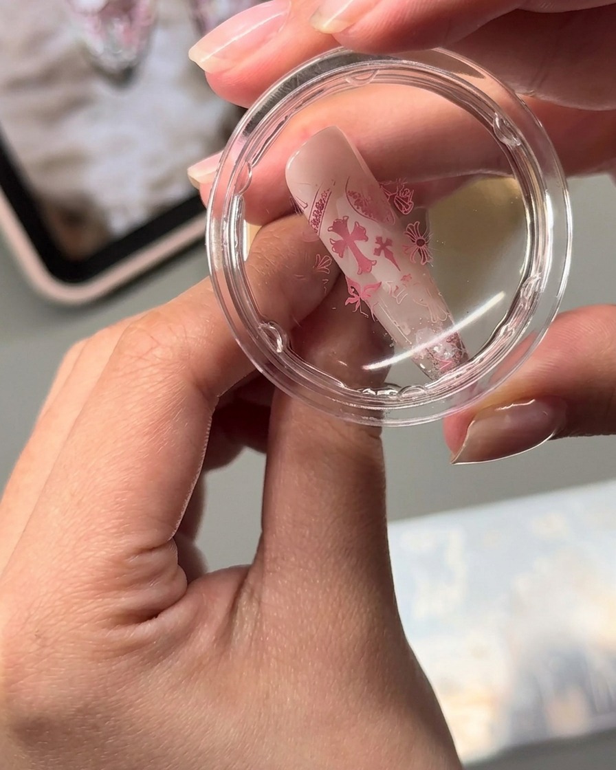 Un sello de gelatina transparente transfiriendo diseños de arte de uñas estampados en rosa sobre la superficie de una uña en forma de almendra.
