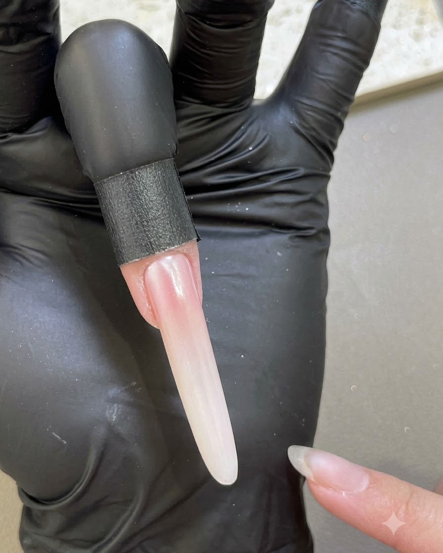 Una uña extendida que muestra un acabado liso y perlado después de sellar con gel base a lo largo de los bordes.