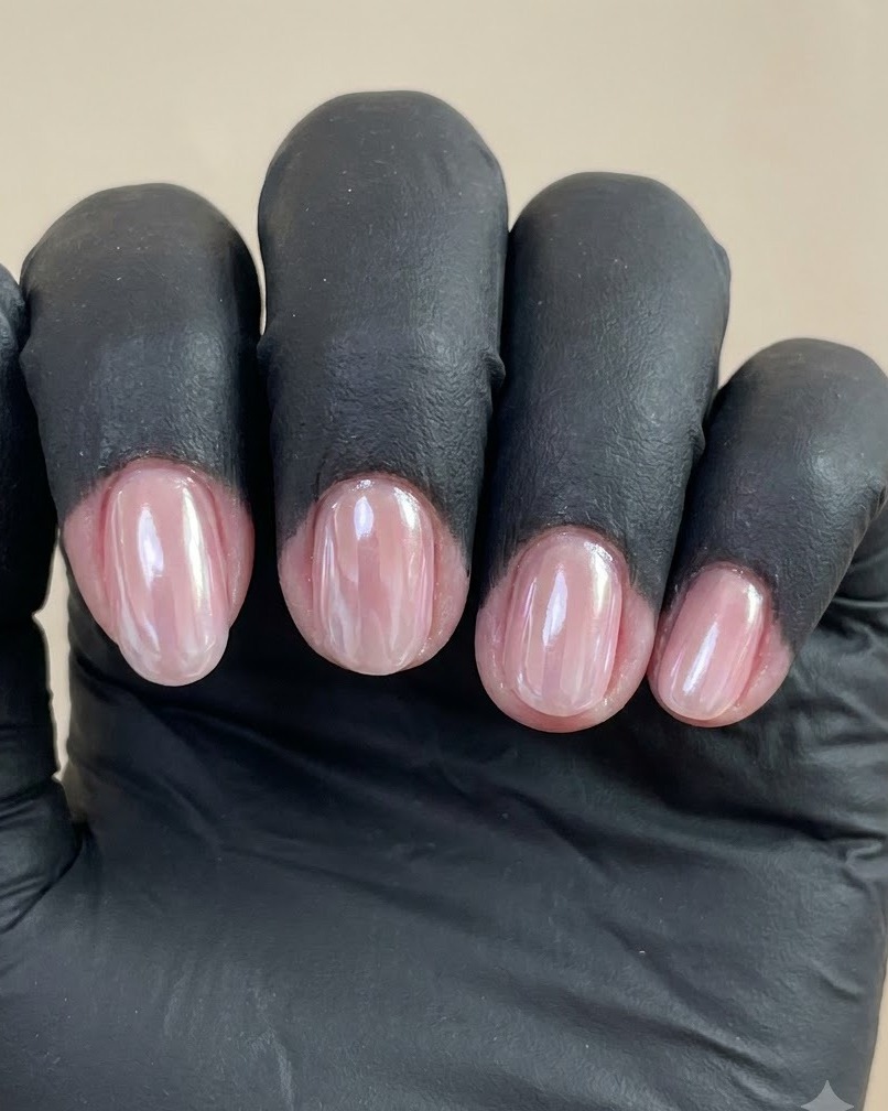 Una vista cercana de una mano enguantada mostrando cuatro uñas manicuradas con un acabado cromo perlado brillante contra un fondo liso.