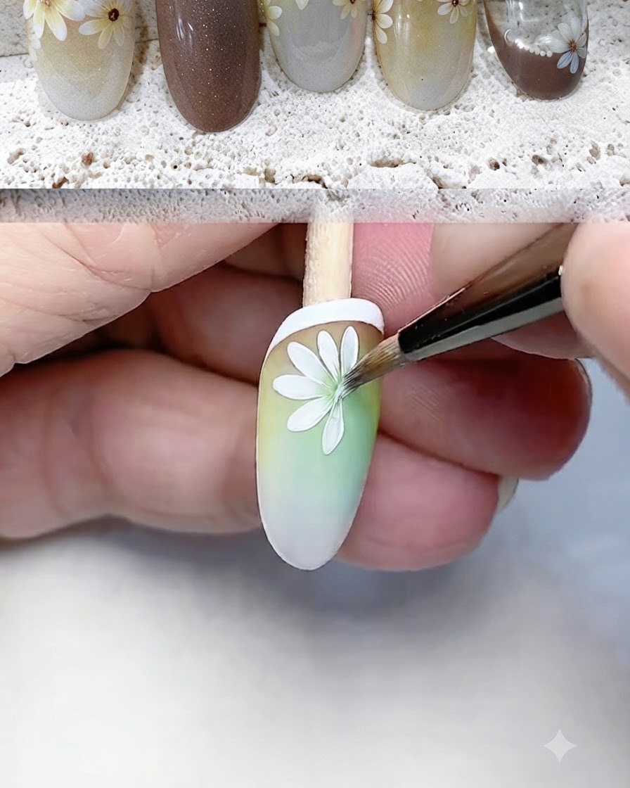 Un pincel delineador fino pintando y definiendo cuidadosamente los pétalos blancos de la margarita en la punta de una uña con degradado.