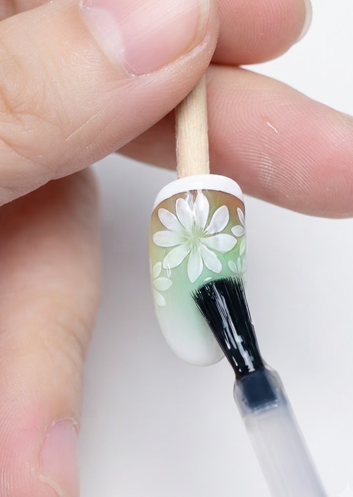 Un pincel aplicando una capa superior mate sobre el nail art de margaritas ya completado.