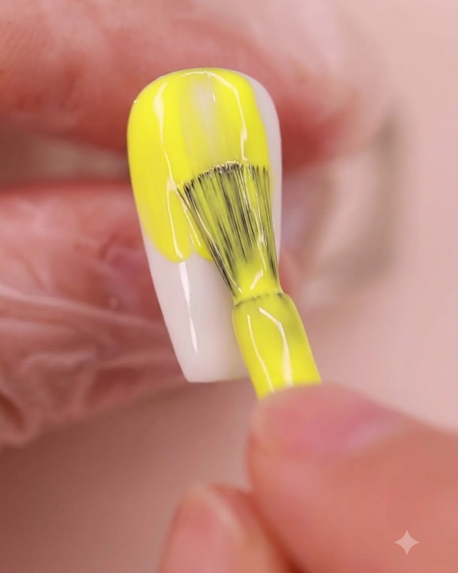 Un pincel de uñas aplicando un esmalte en gel amarillo vibrante de manera uniforme sobre una uña en forma de almendra.