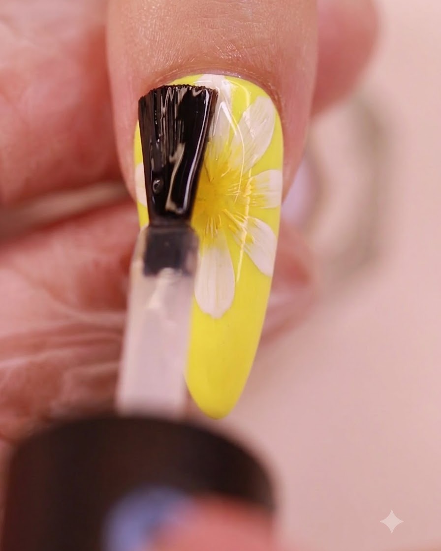 Un pincel aplicando una capa transparente de top coat sin residuos sobre el diseño pintado de uñas de margaritas.