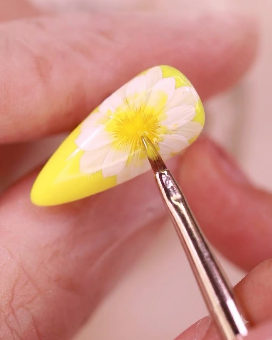 Un pincel de detalles finos aplicando un top coat transparente sobre un diseño de uñas floral.