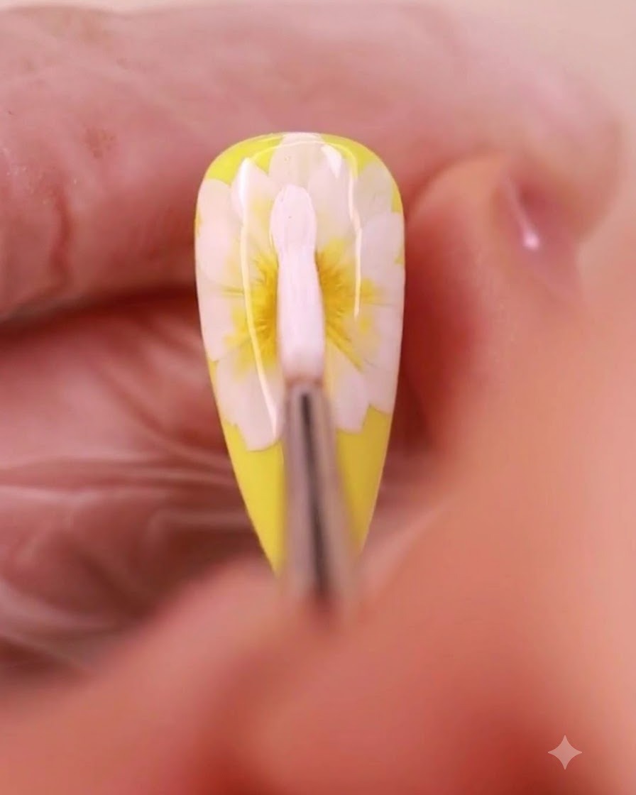 Un pincel de arte de uñas aplicando gel blanco para formar una tercera capa de pétalos en un diseño de margarita.