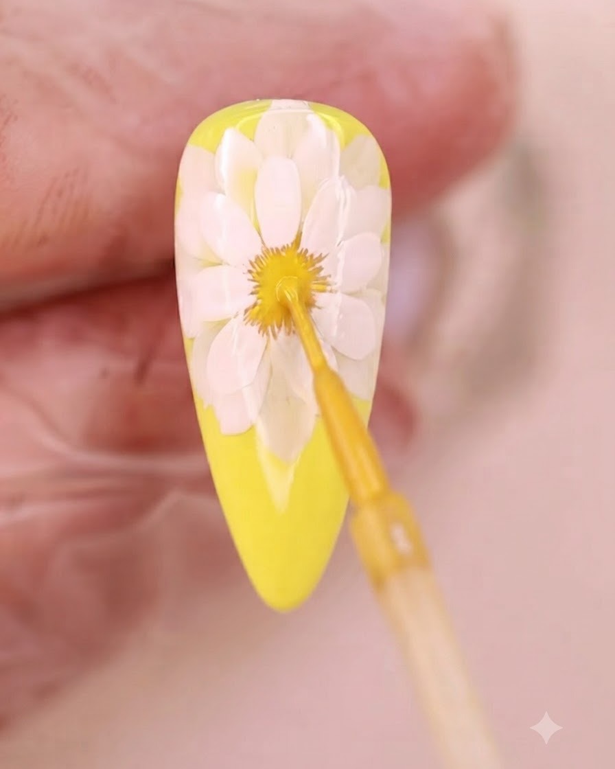 Un pincel fino aplicando líquido amarillo en el centro difuminado de la flor.