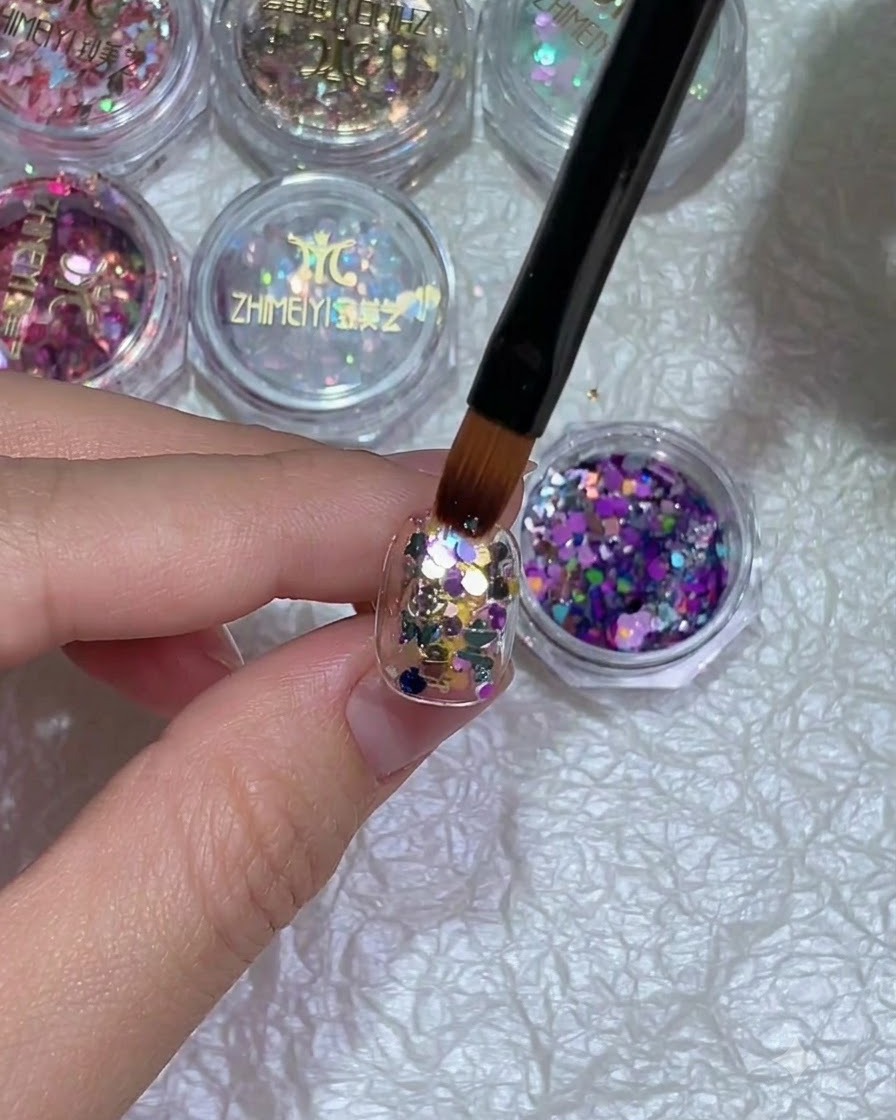 Un primer plano de una mano con nail art de purpurina colocada bajo una lámpara de curado.