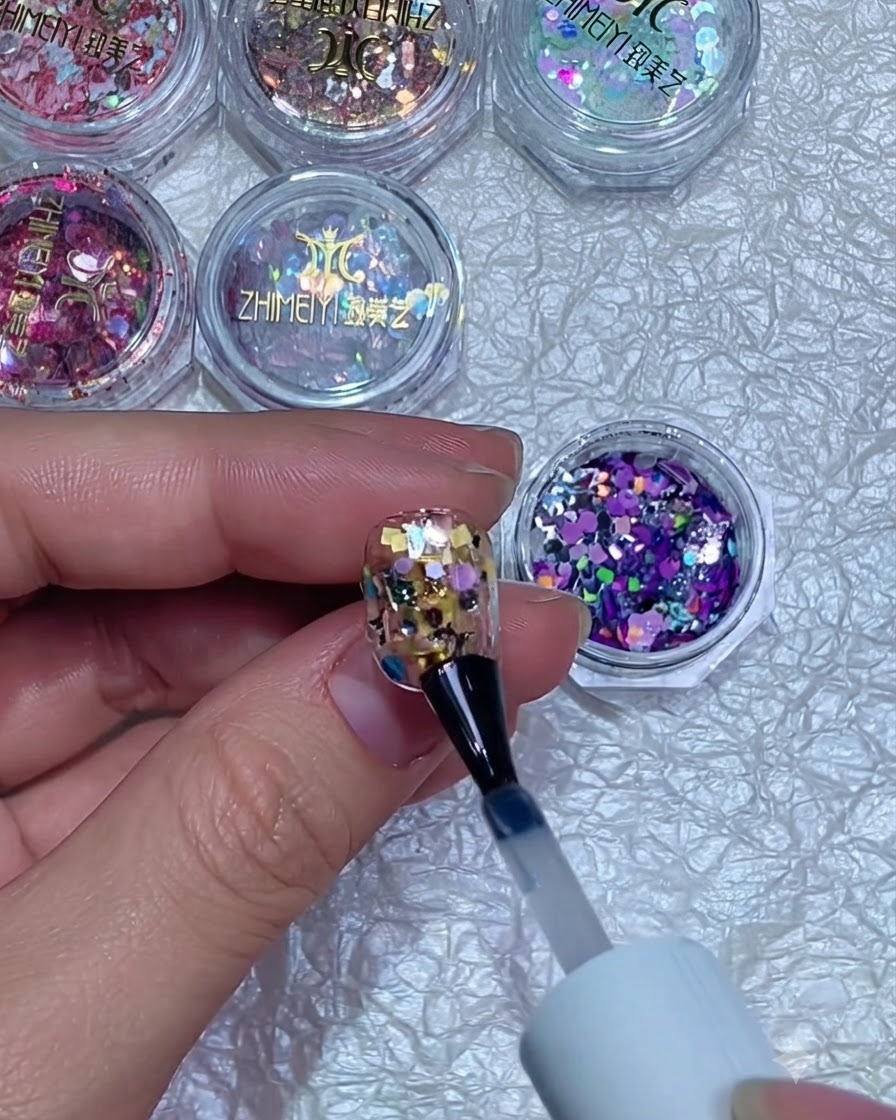 Un pulidor de uñas suavizando la superficie de una uña con purpurina encapsulada y curada.