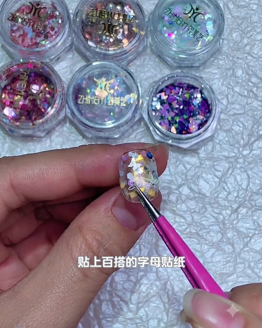 Unas pinzas colocando un pequeño sticker de letra blanca sobre la superficie decorada de una uña de gel.