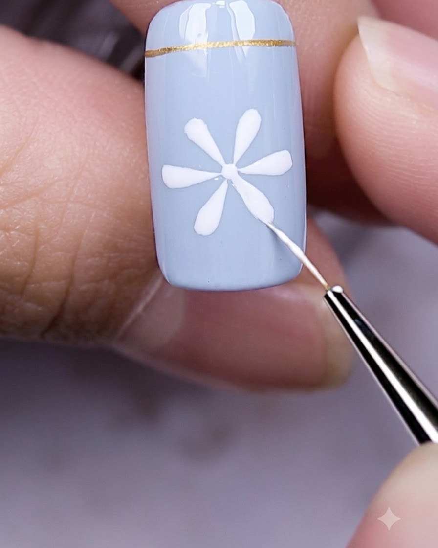 Dedos con una uña azul y diseño de margarita blanca reposando bajo una lámpara LED UV para uñas.
