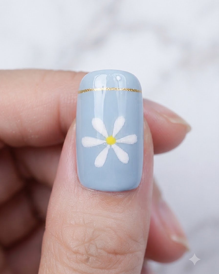 Un pincel aplicando una capa superior transparente y brillante sobre una uña azul terminada con un diseño de margarita.