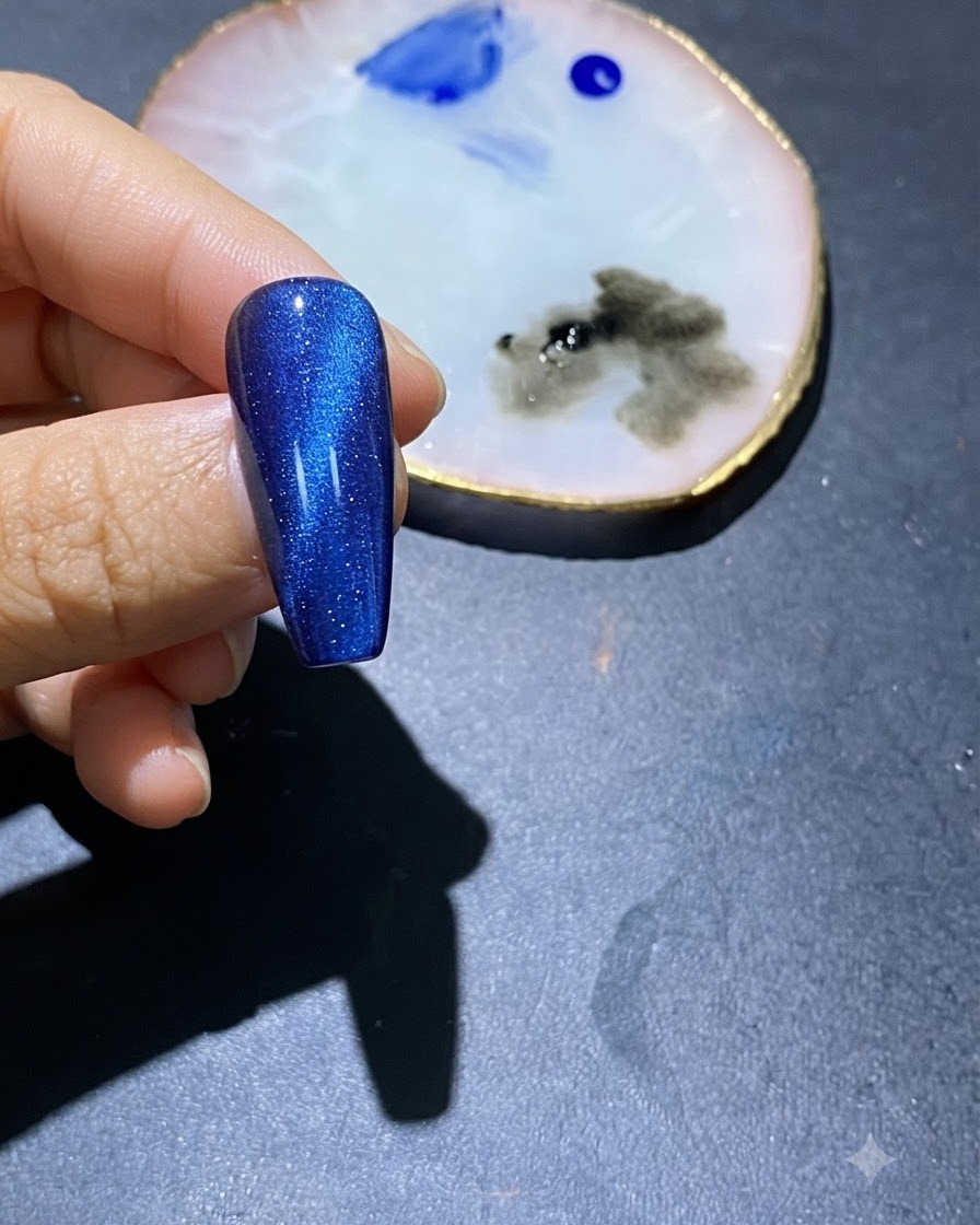 Un primer plano de una uña de gel azul ojo de gato con puntos de esmalte azul en el centro y una paleta de arte cerca.