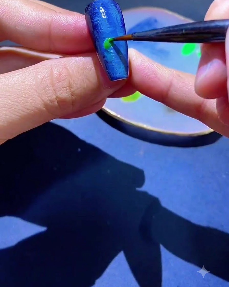 Un pincel delineador fino aplicando un punto de esmalte en gel verde sobre una uña texturizada azul.
