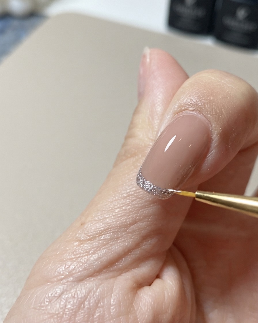 Un pincel fino de nail art perfilando y perfeccionando el borde de un diseño brillante de punta cat-eye.