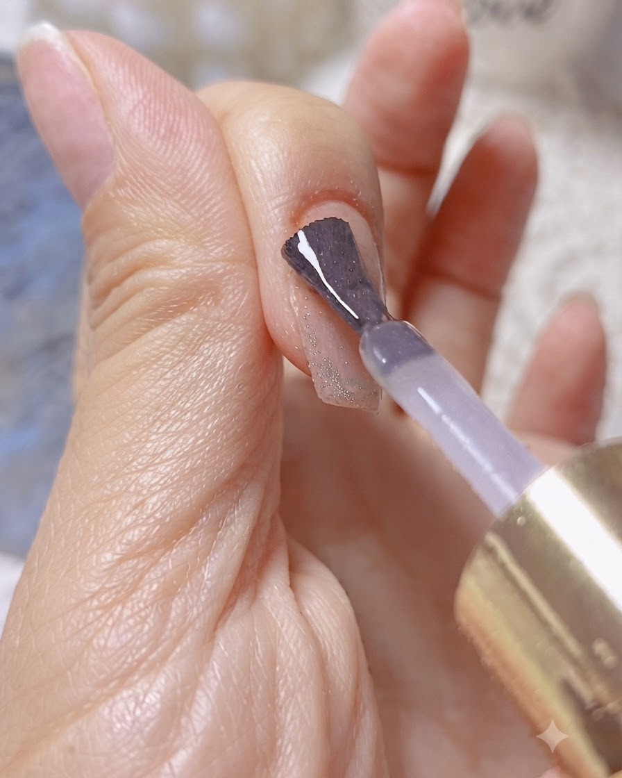 Un pincel aplicando gel constructor o de refuerzo transparente sobre una uña brillante con efecto cat-eye.