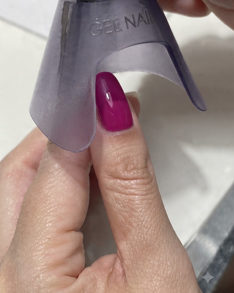 Una lámpara UV/LED morada portátil curando una uña de color magenta oscuro vibrante o azul bajo luz brillante.