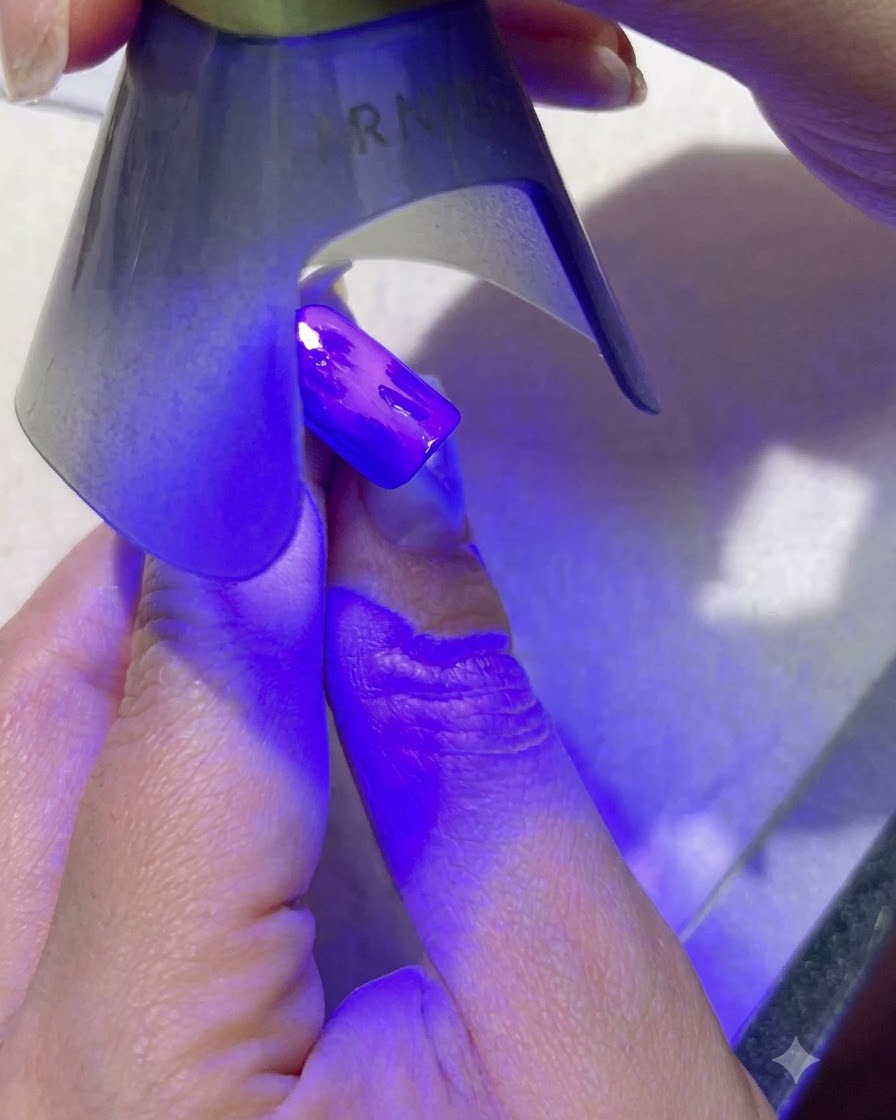 Una lámpara UV morada portátil curando un nail art de hojas verde oscuro en una uña pintada de azul.