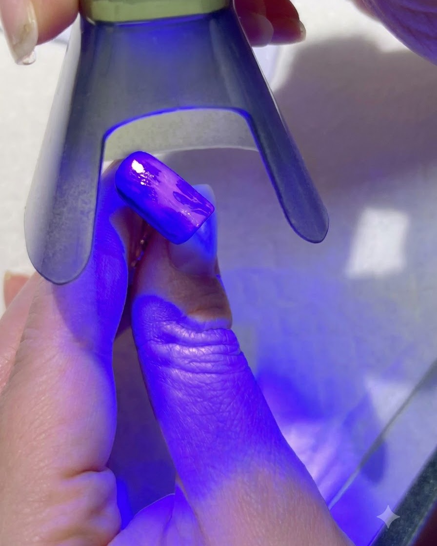 Una lámpara UV morada curando los detalles de hojas verde claro en una uña pintada.