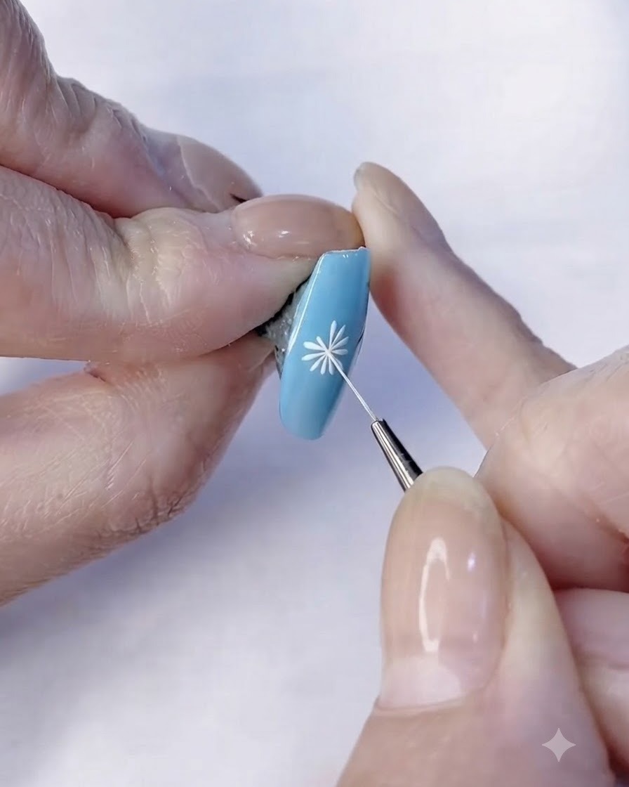 Un pincel fino terminando los detalles de los pétalos blancos de un diseño de nail art de margarita.