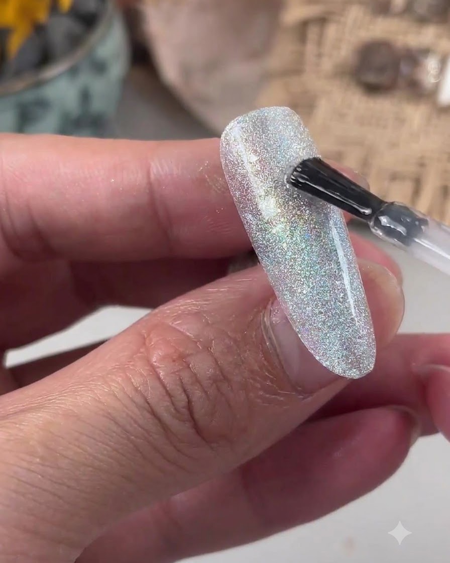 Un pincel aplicando gel nivelador transparente sobre una superficie de uña con purpurina.