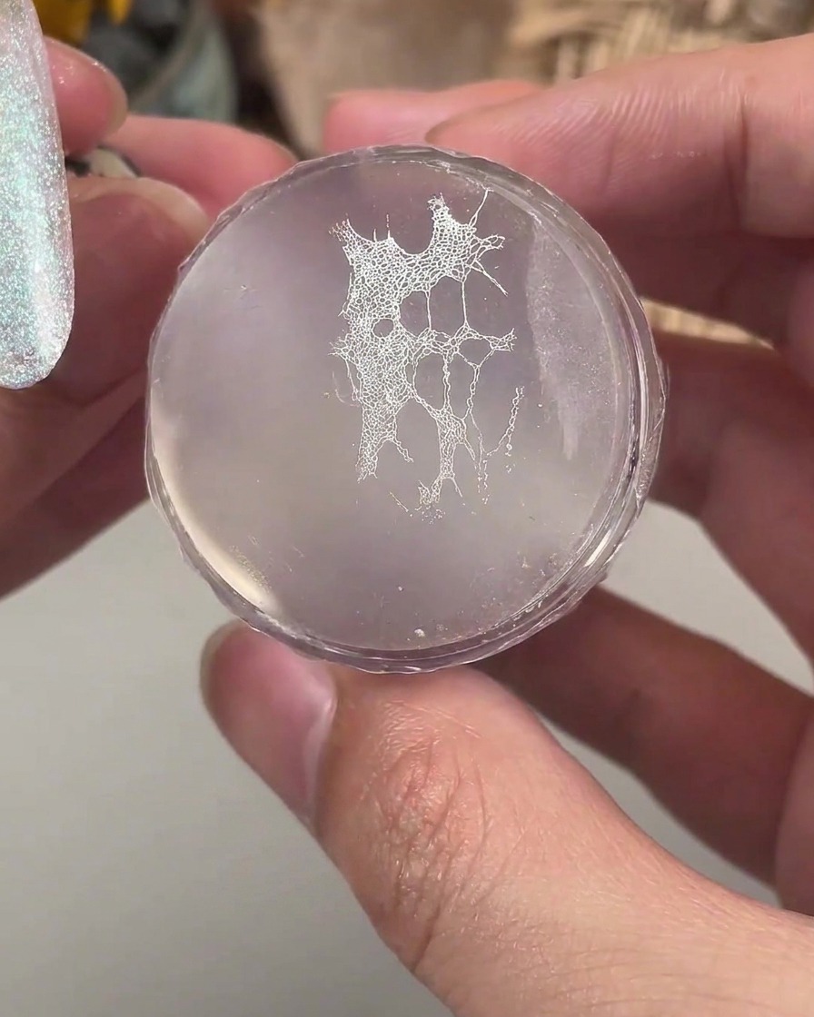 Un sello de silicona transparente que sostiene un patrón de encaje blanco fino listo para transferirse a una uña manicurada.