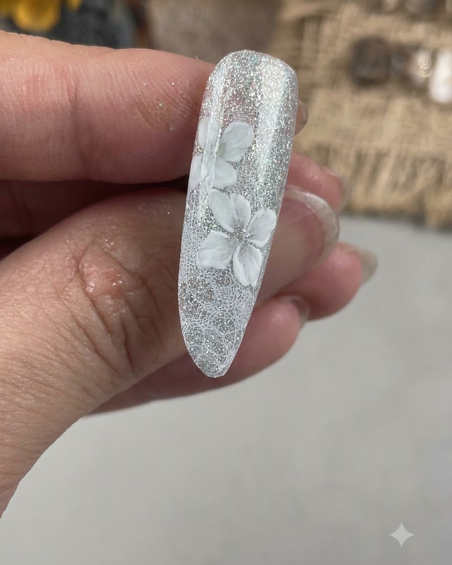 Un primer plano de una uña que muestra una segunda capa de pétalos blancos pintados desalineados de la base floral inicial.