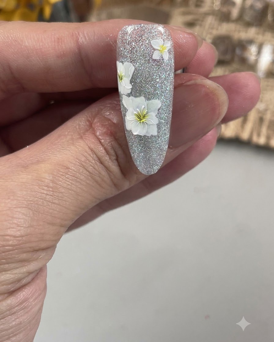 Vista en primer plano de un pincel de nail art fino delineando los delicados pétalos de una flor blanca en una uña texturizada.
