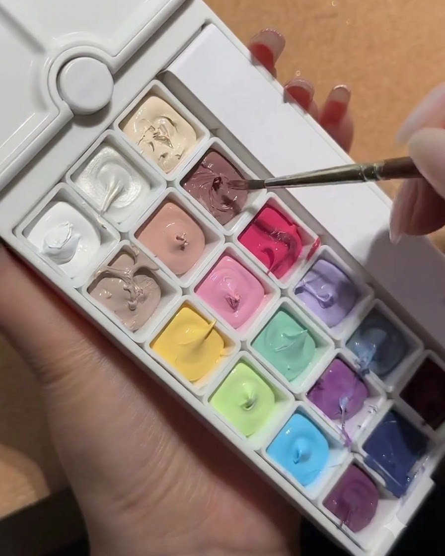 Un pincel de uñas sumergiéndose en una paleta que contiene un compartimento cuadrado de gel melocotón blanco nude.