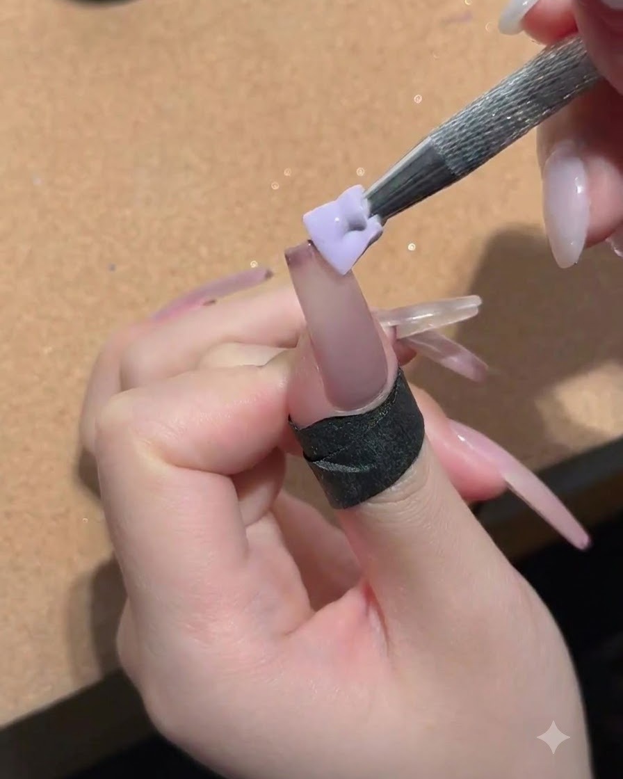 Una pequeña esponja sostenida por una herramienta de metal aplicando gel melocotón nude en la superficie de la uña.