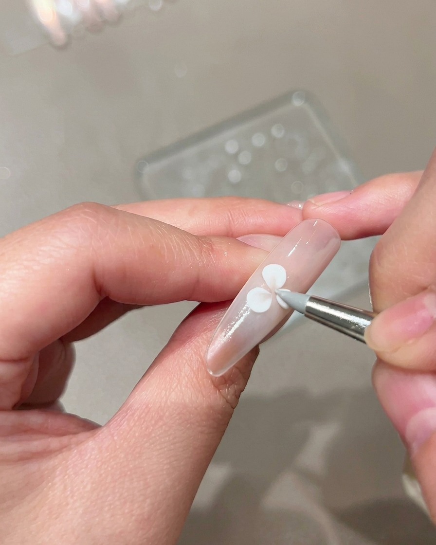 Un pincel de escultura de silicona presionando y moldeando un pétalo de gel blanco en una uña nude manicurada.