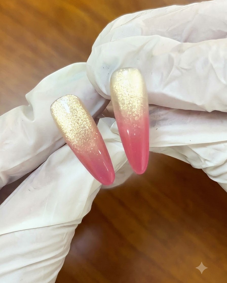 Un pincel aplicando una capa superior transparente sobre un diseño de uñas degradadas cat-eye de rosas al atardecer y oro.