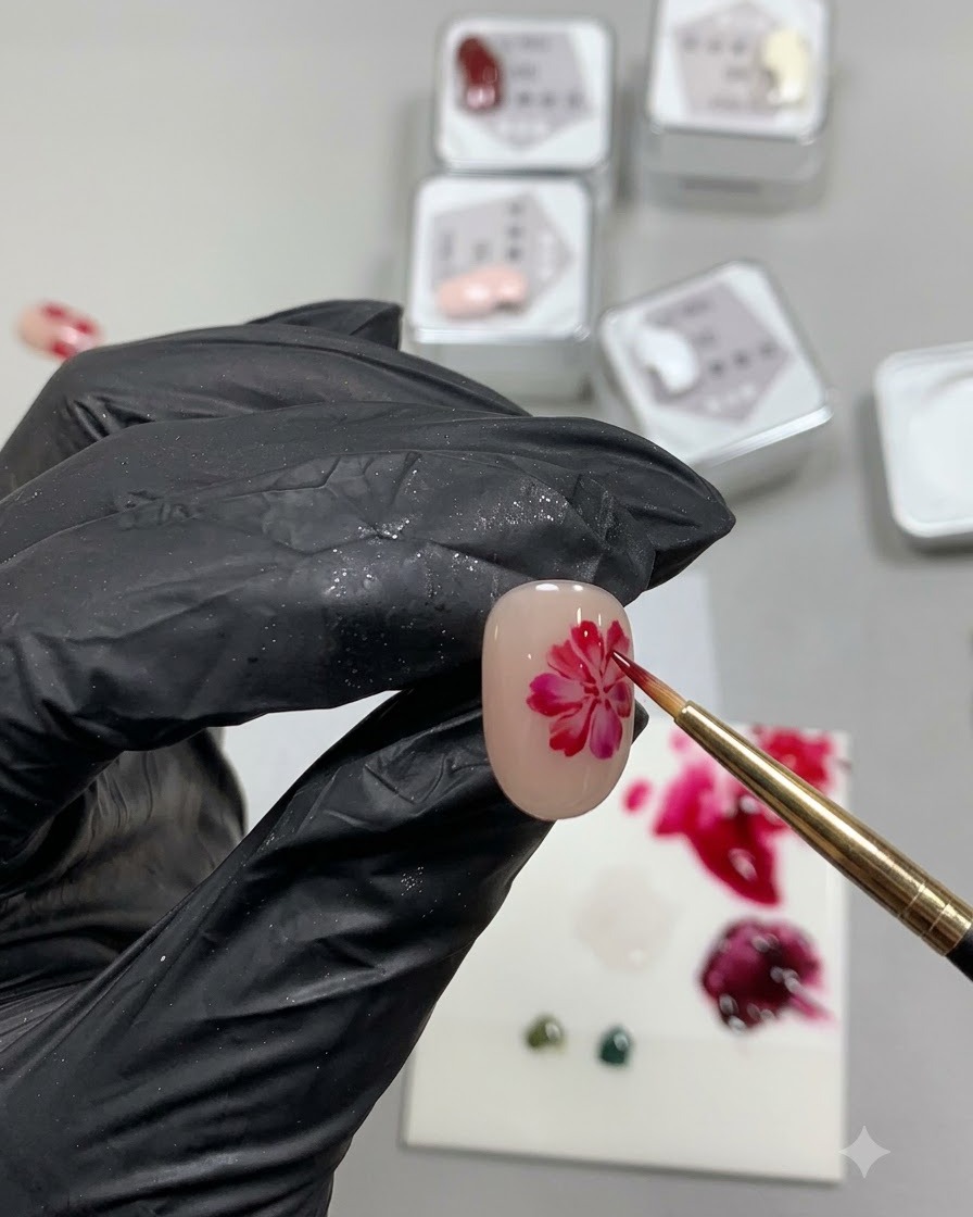 Un pincel de detalle fino pintando un círculo rojo suave, irregular y traslúcido que se asemeja a la base de un pétalo de rosa en una uña nude.